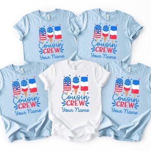 May include: Light blue and white t-shirts with a popsicle graphic in red, white, and blue. The text "Cousin Crew" and "Your Name" are printed below the popsicle design. The shirts are short-sleeved.