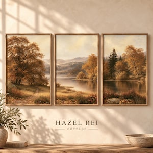 Peut inclure: Un ensemble de trois cadres muraux représentant un paysage automnal serein avec des arbres aux tons brun doré, un lac calme et des collines. L'œuvre présente des couleurs chaudes et terreuses ainsi qu'une atmosphère douce. Le texte Hazel Rei Cottage est visible.