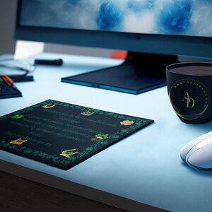 Puede incluir: Una alfombrilla de ratón negra con un diseño de trébol verde y una cita sobre la buena fortuna. La alfombrilla de ratón está sobre un escritorio azul con una taza de café negra y un ratón de ordenador blanco.