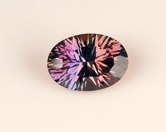 May include: An oval-cut gemstone with a complex, faceted design. The gem features a gradient of colors, transitioning from deep purple to pink and black. The stone is set against a neutral background.