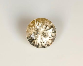 May include: A round, faceted gemstone with a golden hue. The gem has multiple facets that reflect light, creating a sparkling effect. The gemstone is set against a plain white background.