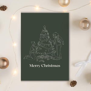 May include: A dark green Christmas card featuring a white line drawing of two people decorating a Christmas tree. The words "Merry Christmas" are printed at the bottom. The card is surrounded by baubles and pine cones.
