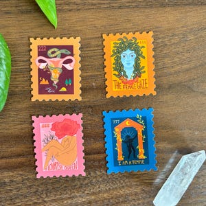 Peut inclure: Quatre autocollants colorés en forme de timbre avec des motifs uniques. L'un représente un utérus avec un serpent, un autre Méduse, un troisième une figure avec une tête de fleur et le dernier un temple. Chacun a un numéro différent.