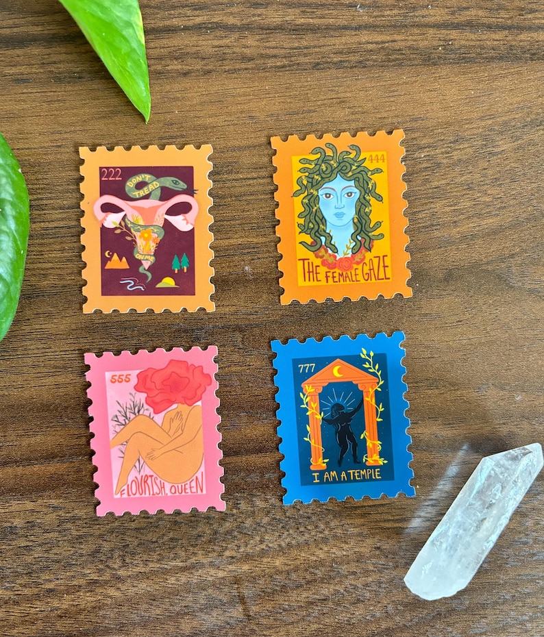 Four colorful feminist art stickers in the shape of postage stamps, each featuring empowering designs and phrases like “Don’t Tread on Me,” “The Female Gaze,” “Flourish, Queen,” and “I Am a Temple.” Stickers are arranged on a wood surface with a crystal point and green leaves.