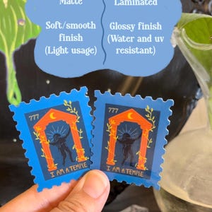 May include: Two blue stickers with a stamp design. Each sticker features a temple illustration with the text "I AM A TEMPLE". The stickers are held by a person. The image also shows text about matte and laminated finishes.