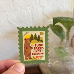 K&ouml;nnte beinhalten: Eine gr&uuml;ne Briefmarke mit einem braunen B&auml;ren, der eine Blume h&auml;lt, mit dem Text "Fund Parks Not Billionaires". Die Briefmarke zeigt auch eine gelbe Sonne, gr&uuml;ne B&auml;ume und rote Pilze. Die Briefmarke ist 10 Cent wert.