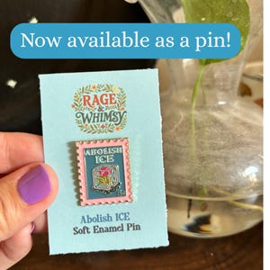 May include: A soft enamel pin with the text "ABOLISH ICE" inside a pink postage stamp design. The pin is on a light blue card with the text "RAGE & WHIMSY" and "Abolish ICE Soft Enamel Pin". The image also includes the text "Now available as a pin!"