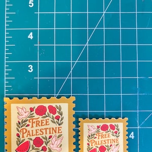 May include: Two postage stamps with a yellow border and a cream-colored center. The stamps feature the text "Free Palestine" with illustrations of doves, flowers, and a watermelon. The word "Forever" is printed at the bottom of each stamp.