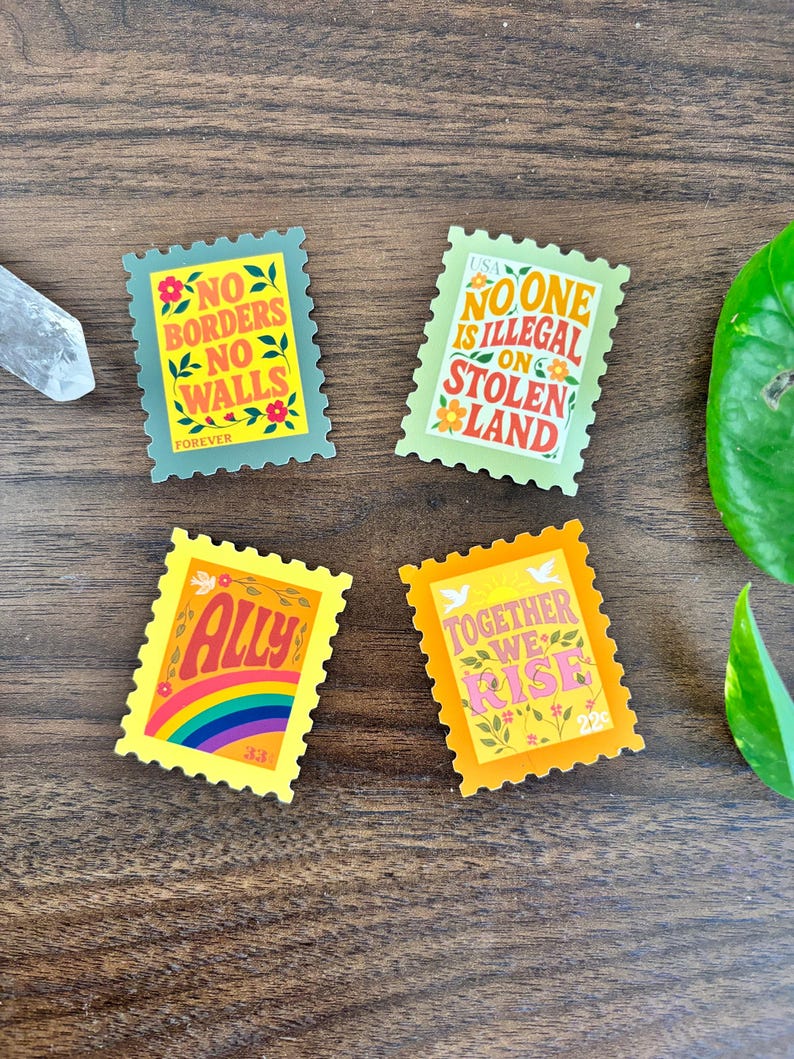 a set of four stamp-shaped stickers. one sticker reads “no borders no walls.” Another sticker reads “no one is illegal on stolen land.” Another sticker reads “together we rise.” and the last one reads “ally” featuring a rainbow and a dove.