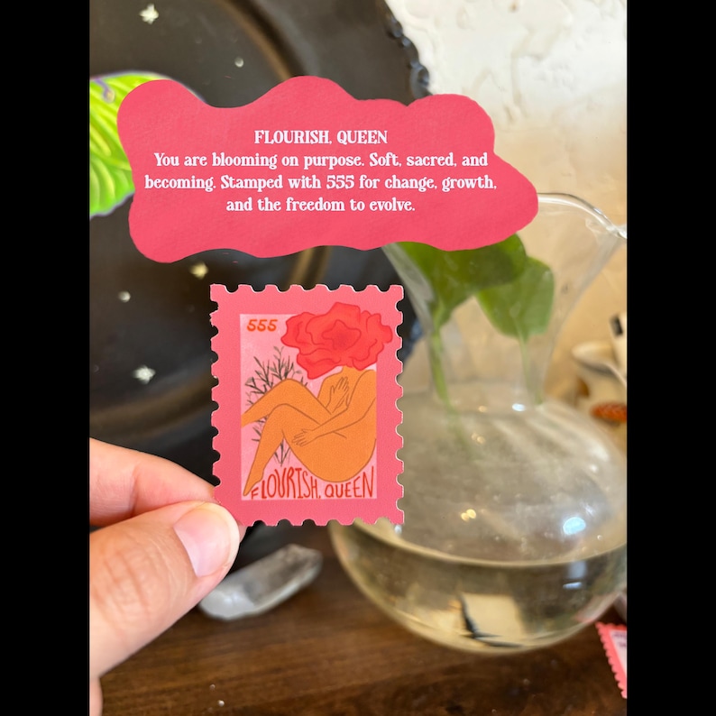 May include: A pink stamp with the text "FLOURISH QUEEN" and the number "555". The stamp features an illustration of a figure with a flower for a head. The stamp is held in front of a glass vase with water and a plant.
