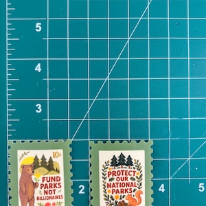 K&ouml;nnte beinhalten: Zwei Briefmarken mit gr&uuml;nen R&auml;ndern. Eine zeigt einen B&auml;ren, B&auml;ume und den Text "FUND PARKS NOT BILLIONAIRES". Die andere zeigt ein Eichh&ouml;rnchen, B&auml;ume und den Text "PROTECT OUR NATIONAL PARKS". Beide Briefmarken haben ein Vintage-Design.