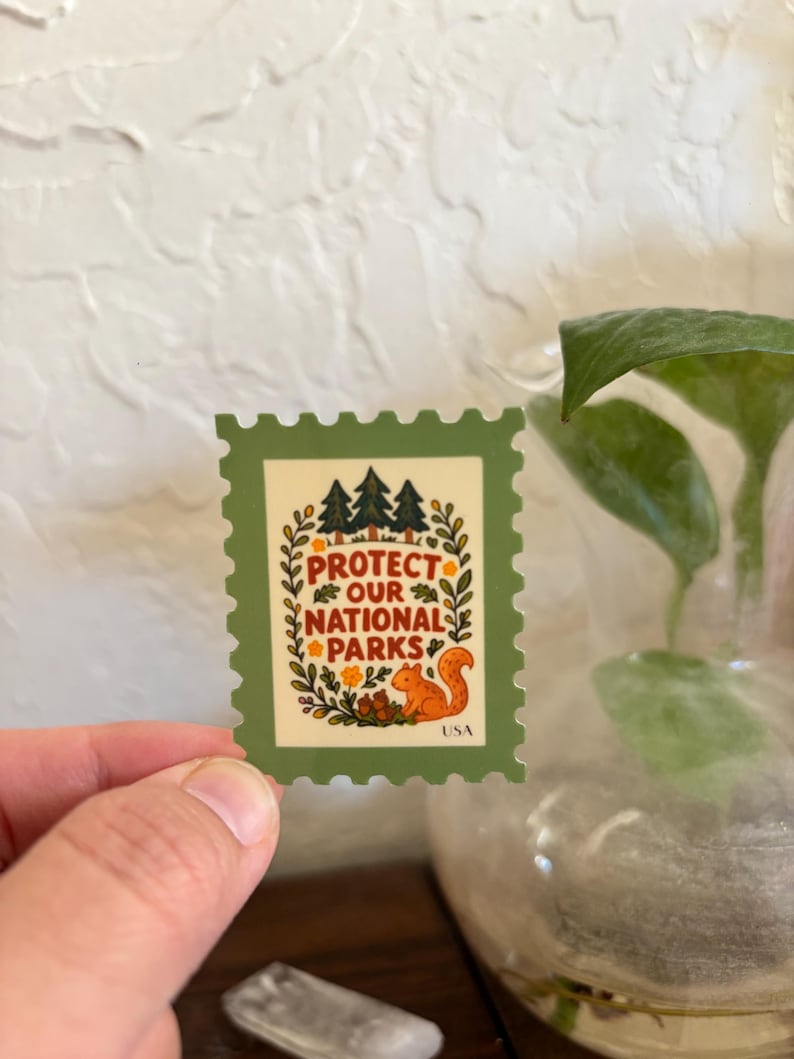 K&ouml;nnte beinhalten: Ein gr&uuml;ner und cremefarbener Aufkleber in Form einer Briefmarke. Der Aufkleber zeigt den Text "PROTECT OUR NATIONAL PARKS" mit einem Eichh&ouml;rnchen und B&auml;umen. Das Wort "USA" steht unten.