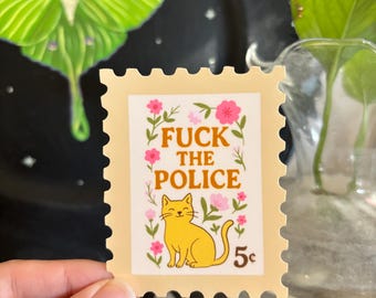 Może przedstawiać: Projekt znaczka pocztowego w kolorze beżowym z napisem "FUCK THE POLICE" i ilustracją żółtego kota. Różowe kwiaty i zielone liście otaczają tekst i kota. Znaczek ma również wartość "5¢".