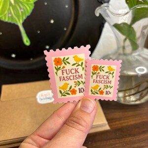 a stamp shaped sticker featuring folk art style birds, flowers and leaves. The text reads “fuck fascism.”