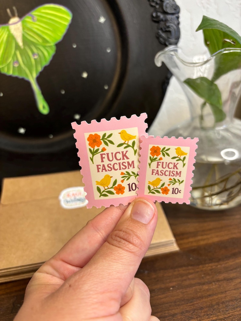 a stamp shaped sticker featuring folk art style birds, flowers and leaves. The text reads “fuck fascism.”