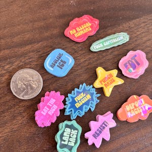 May include: A collection of colorful, die-cut stickers with various political slogans and phrases. The stickers are in various shapes, including clouds, stars, and speech bubbles. A U.S. quarter is included for size reference.