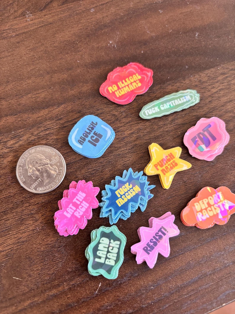 May include: A collection of colorful, die-cut stickers with various political slogans and phrases. The stickers are in various shapes, including clouds, stars, and speech bubbles. A U.S. quarter is included for size reference.