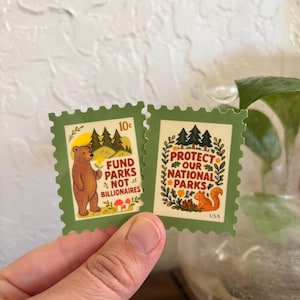 May include: Two green postage stamp stickers. One features a bear with text reading "Fund Parks Not Billionaires." The other says "Protect Our National Parks" with a squirrel and floral design. Both have a 10¢ value.