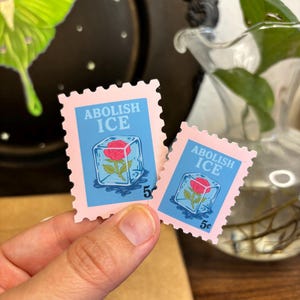 a stamp shaped sticker featuring a melting ice cube with a rose inside. text reads “abolish ice.”