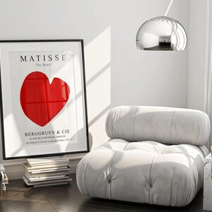 K&ouml;nnte beinhalten: Ein wei&szlig;er, gesteppter Sessel mit einem gro&szlig;en, roten herzf&ouml;rmigen Druck in einem schwarzen Rahmen. Der Druck lautet "MATISSE The Heart" und "BERGGREEN & CIE".