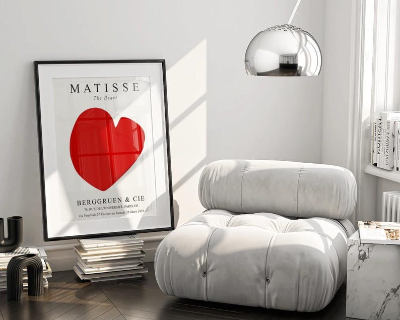 K&ouml;nnte beinhalten: Ein wei&szlig;er, gesteppter Sessel mit einem gro&szlig;en, roten herzf&ouml;rmigen Druck in einem schwarzen Rahmen. Der Druck lautet "MATISSE The Heart" und "BERGGREEN & CIE".