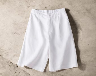 May include: White shorts with a button closure and pleats. The shorts have a tailored design and a classic look. The garment is made of a smooth, opaque fabric. The shorts are suitable for warm weather.