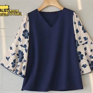 Peut inclure: Un chemisier bleu marine à col en V avec des manches évasées. Les manches présentent un motif floral crème avec des fleurs et des feuilles bleu marine. Le chemisier est suspendu à un cintre en bois. Le texte "MINIMALIST APPAREL" est visible.