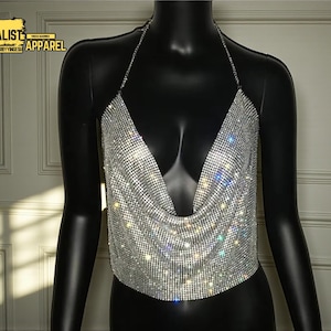 Op de afbeelding: Een zilveren, sprankelende haltertop met een diepe V-hals. De top is gemaakt van een mesh materiaal bedekt met kleine, reflecterende strass steentjes. De woorden "MINIMALIST APPAREL" staan in een gele rechthoek linksboven.