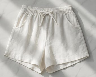 May include: Off-white linen shorts with an elastic waistband and drawstring. The shorts have two front pockets and a relaxed fit. The fabric appears to be lightweight and suitable for warm weather. The shorts are laid flat on a marble surface.