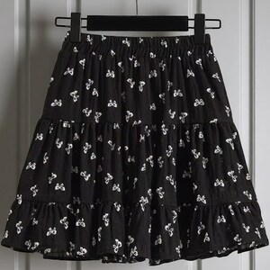 May include: Black tiered skirt with white butterfly pattern. The skirt is hanging on a black hanger. The skirt has a ruffled hemline and an elastic waistband.