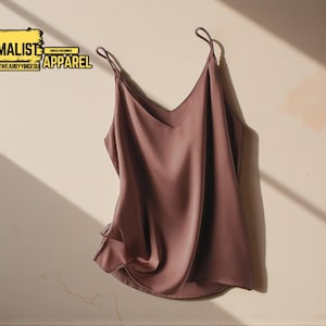 Puede incluir: Un camisola de color malva con finas tiras y cuello en V. La parte superior está hecha de un material sedoso y tiene un diseño fluido y drapeado. Las palabras "MINIMALIST APPAREL" están en un rectángulo amarillo y negro.