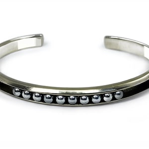 May include: A silver bangle bracelet with a row of small silver beads along the bottom edge.