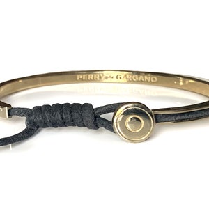 May include: A gold bangle bracelet with a black leather strap and a gold circular charm with a smaller circle in the center. The bracelet is engraved with the text "Perry Gargano".