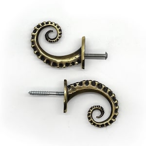 May include: Two brass curtain tiebacks in the shape of a curled tentacle. Each tieback has a screw for mounting.