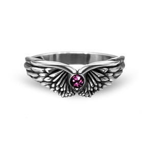 Op de afbeelding: Een zilveren ring met een engelenvleugelontwerp. De ring heeft gedetailleerde veren en een centrale, ronde, roze edelsteen. De vleugels wikkelen zich om de vinger, waardoor een unieke en elegante uitstraling ontstaat. De ring staat tegen een witte achtergrond.