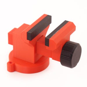 May include: A red plastic mini vise with black rubber jaws and a black plastic knob. The vise is mounted on a round base.