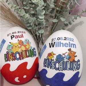 Pode incluir: Dois ovos de P&aacute;scoa grandes e decorados com o texto "27.08.2022" e "Einschulung". Um ovo &eacute; vermelho com um design de Pokemon e o nome "Paul". O outro ovo &eacute; azul com um design de desenho animado e o nome "Wilhelm".