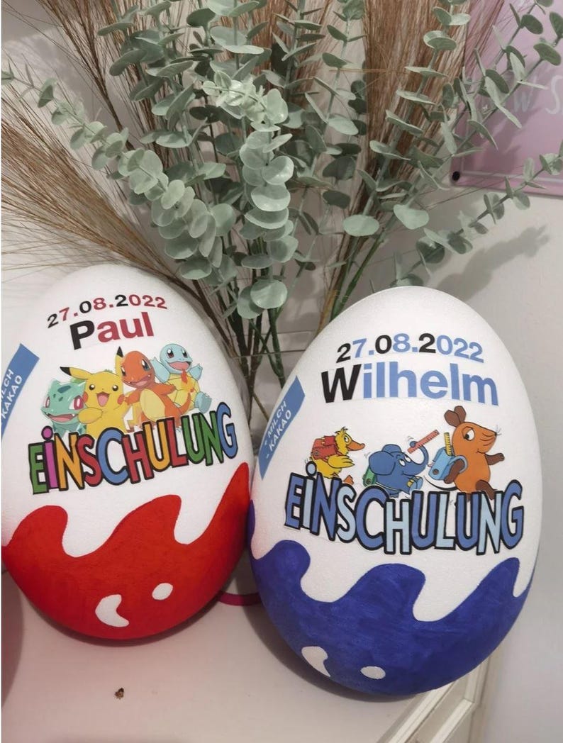 Pode incluir: Dois ovos de P&aacute;scoa grandes e decorados com o texto "27.08.2022" e "Einschulung". Um ovo &eacute; vermelho com um design de Pokemon e o nome "Paul". O outro ovo &eacute; azul com um design de desenho animado e o nome "Wilhelm".