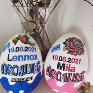 Pode incluir: Dois ovos brancos decorados com o texto "19.08.2021" e os nomes "Lennox" e "Mila" neles. Os ovos s&atilde;o decorados com um tema Minecraft e um tema LOL Surprise. O texto "Einschulung" est&aacute; em ambos os ovos.