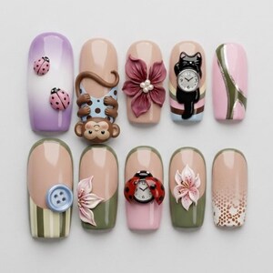 Könnte beinhalten: Eine Sammlung von zehn künstlichen Nägeln mit verschiedenen Designs. Die Designs umfassen Marienkäfer, einen Affen, eine Blume, eine schwarze Katze mit einer Uhr, Streifen, einen Knopf und ein Spitzenmuster. Die Nägel sind in Rosa-, Lila-, Grün- und Beigetönen lackiert.