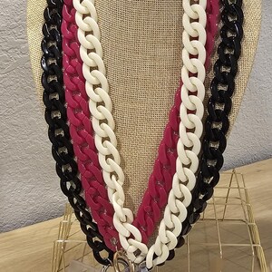 May include: A layered chain necklace with black, white, and pink chunky links. The necklace is displayed on a mannequin and has a gold key ring attached to the bottom.