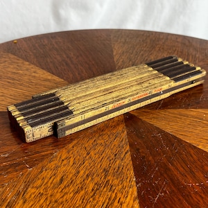 May include: A folded wooden extension rule with a yellow finish and black markings. The tool features the text Lufkin Extension Rule printed on the side, with visible measurements in inches ranging from 1 to 5 on the exposed segment.