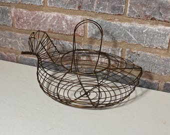 May include: A wire bird-shaped basket with a handle. The basket is made of thin wire and has a rounded shape. The basket is brown in color and has a rustic look.