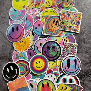 Puede incluir: Una colección de pegatinas de caras sonrientes coloridas con varios diseños. Las pegatinas presentan patrones de arcoíris, psicodélicos y triposos. Algunas son redondas, otras cuadradas o de formas irregulares. La paleta de colores incluye amarillos, azules, verdes y rosas brillantes.