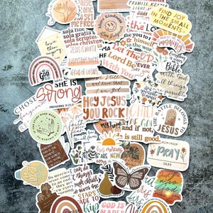 May include: A collection of colorful stickers with inspirational quotes and religious themes. The stickers feature various designs, including rainbows, butterflies, and floral elements, with phrases like "Hey Jesus You Rock!" and "Find Joy in the Small Moments."
