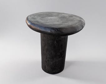 May include: A black, round, mushroom-shaped side table with a smooth, slightly uneven top and a cylindrical base.