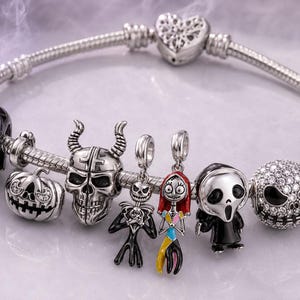 Op de afbeelding: Een zilveren bedelarmband met een collectie horror-bedels, waaronder een non, een pompoen, een schedel met hoorns, Jack Skellington, Sally, een figuur met een masker, een met kristallen ingelegde schedel en een zwarte kat, met hartsluiting.