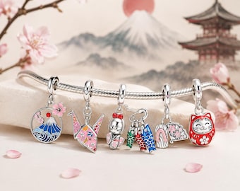May include: A silver charm bracelet featuring six distinct dangling charms: a circular mountain and wave scene with pink flowers, a pink patterned origami crane, a kokeshi doll, three colorful koi fish, a fan with flowers, and a red daruma doll.