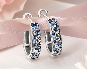 May include: A pair of sterling silver hoop earrings featuring an intricate ocean-themed design with embossed seashells and starfish. The surface is embellished with a gradient of blue and clear cubic zirconia stones and includes an S925 hallmark stamp.
