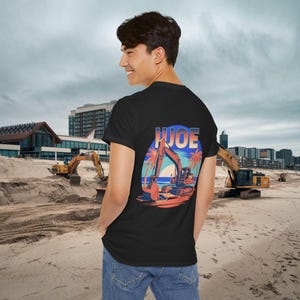 Puede incluir: Camiseta negra con un gráfico de una excavadora de construcción en una playa con palmeras y la palabra "JOE" en letras azules.